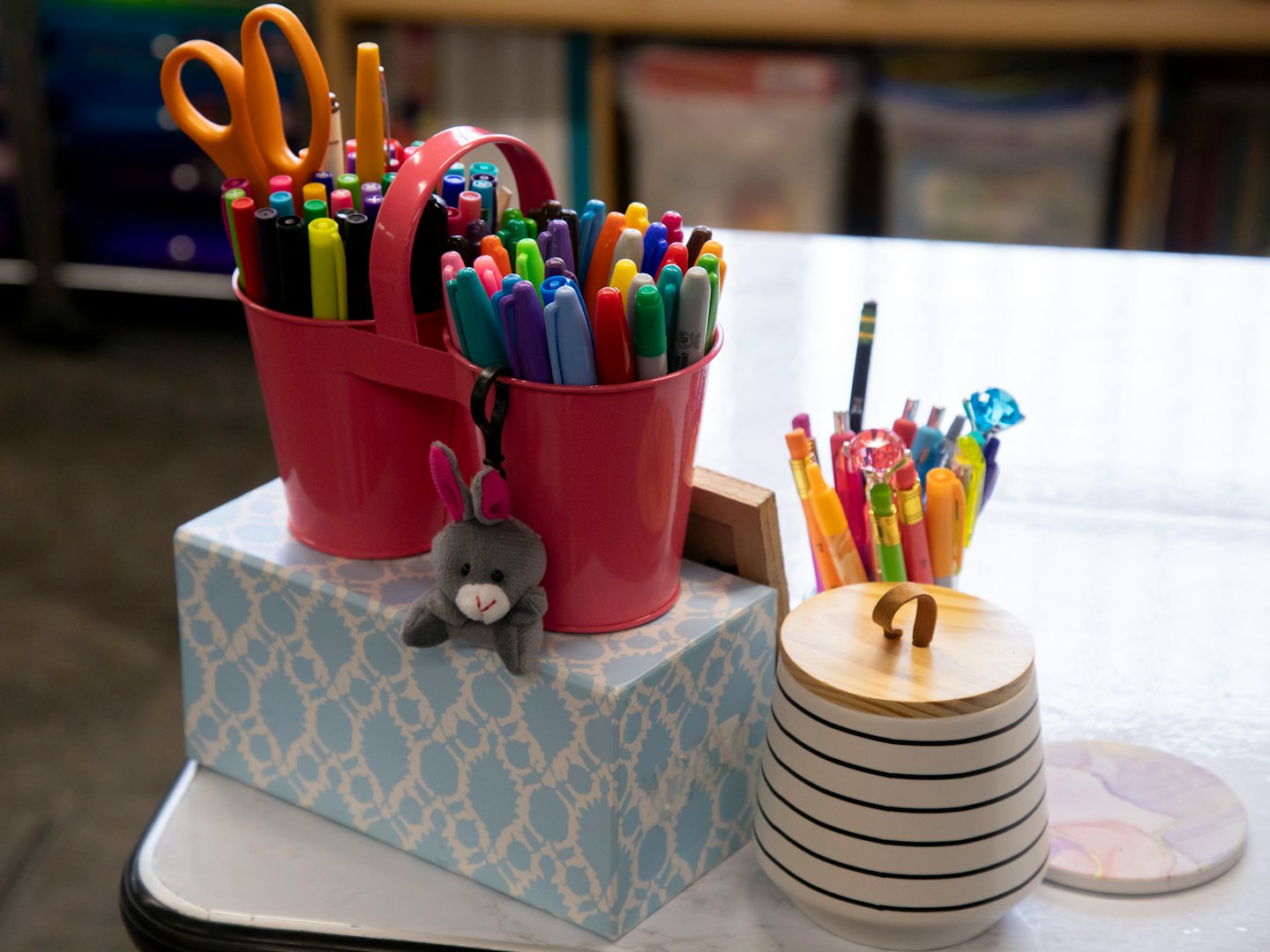 Colorful art and craft supplies in pink buckets on a white table.
