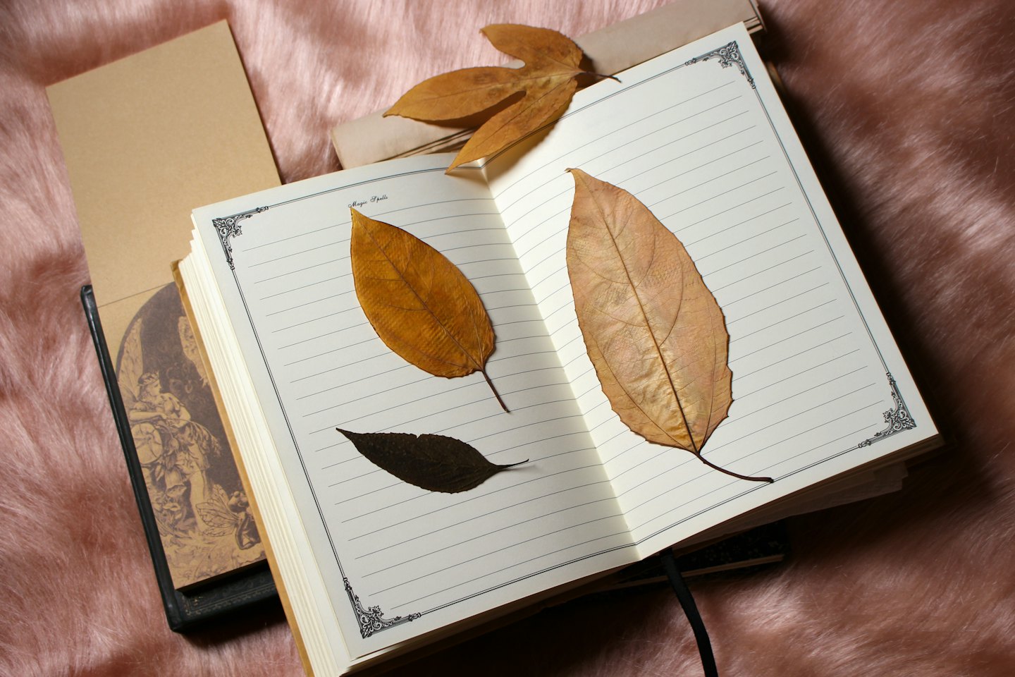 Dried autumn leaves pressed in an open journal on pink faux fur.